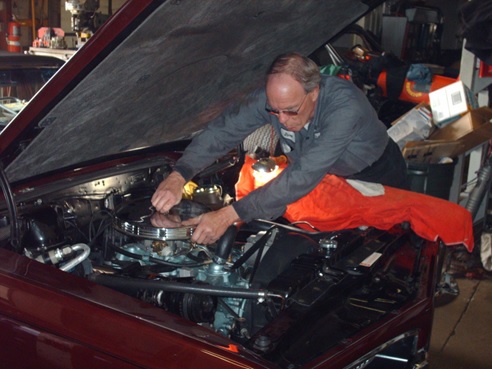Dave Stevens leaning over an open engine bay, working on a classic car.