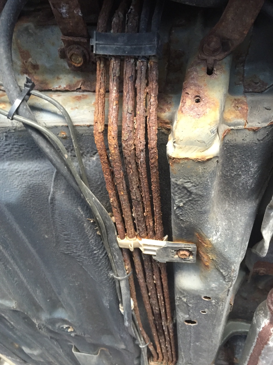 Heavily rusted brake lines under a vehicle.